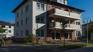 Een meerlaags gebouw met een balkon, een fiets geparkeerd ervoor en een heldere blauwe lucht.