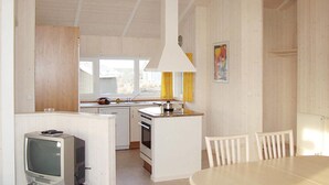 Eine kompakte Küche mit Kochinsel, ein Essbereich mit weißen Stühlen und ein Fernseher in der Ecke.