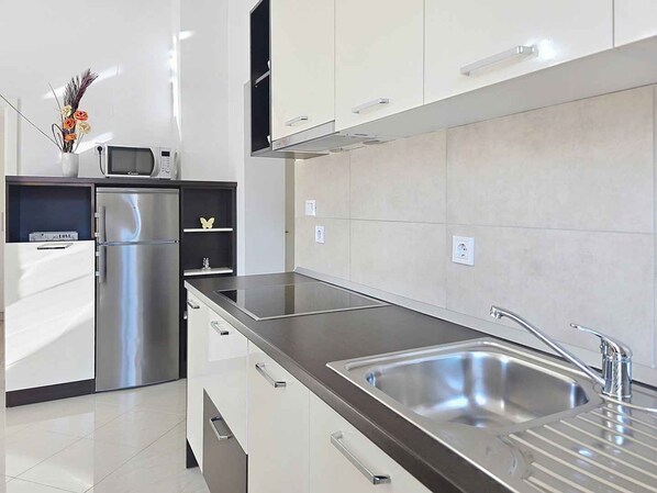 A modern kitchen with stainless steel appliances, a flat sink, and white cabinetry.