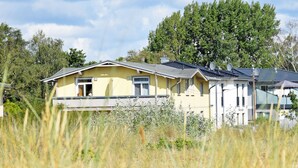 A yellow house with a balcony, surrounded by tall grass and trees. - Vacation apartment 03 with sea view - Strandhaus Göhren 100 m to the beach! (Göhren)