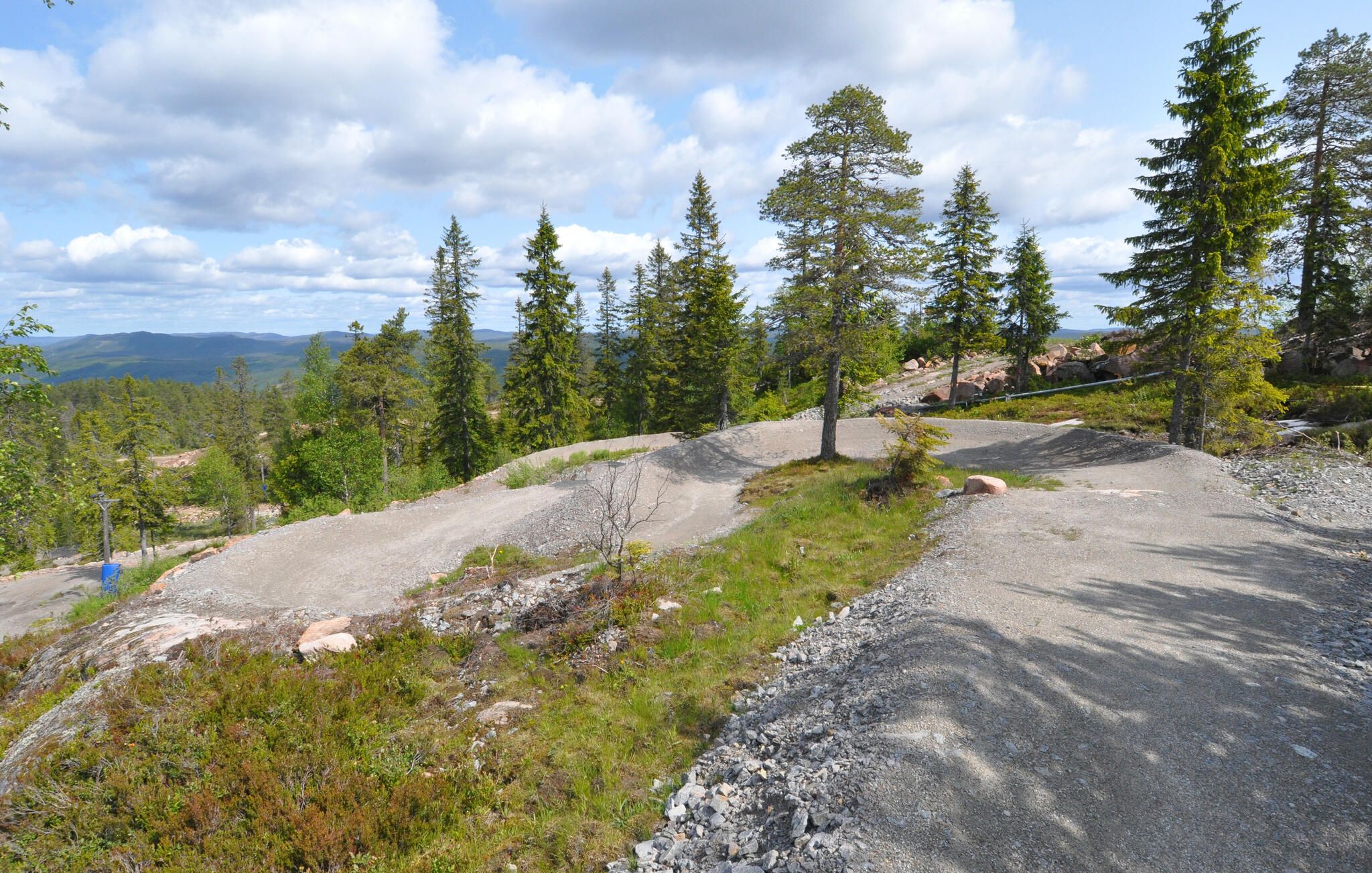 A gravel path surrounded by trees and rocky terrain.