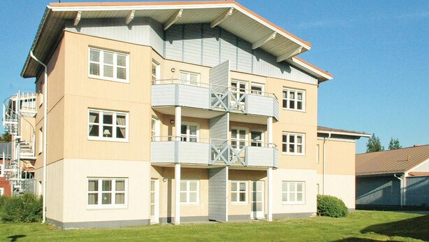 Un edificio residencial de varios pisos con techo plano, balcones y un pequeño jardín delantero.