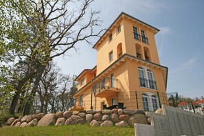 Un immeuble à plusieurs étages, doté d’une façade jaune, de balcons et d’un mur de pierre au premier plan.