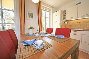 Un coin repas avec une table en bois dressée pour deux personnes, des chaises rouges et une vue sur l’extérieur grâce à de grandes fenêtres.