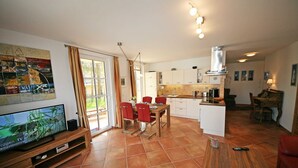 Una cucina moderna con mobili bianchi, un tavolo da pranzo in legno con sedie rosse e un televisore su un supporto in legno.