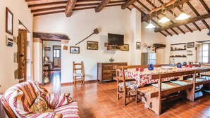 A rustic interior with exposed wooden beams, a dining area with a table set for four, a sofa, and a television mounted on the wall. - Amazing home in Arcidosso GR (Arcidosso GR)