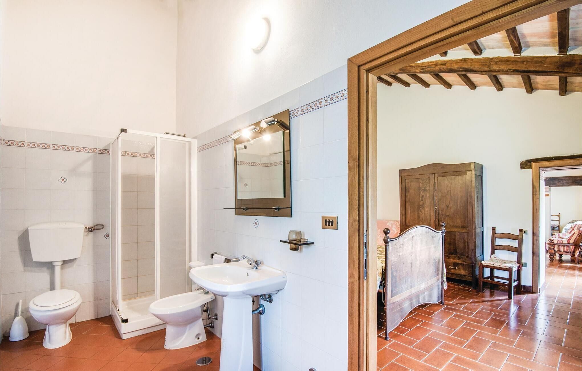 Un baño con inodoro, bidé y lavamanos, ducha y puerta de madera que da a otra habitación.