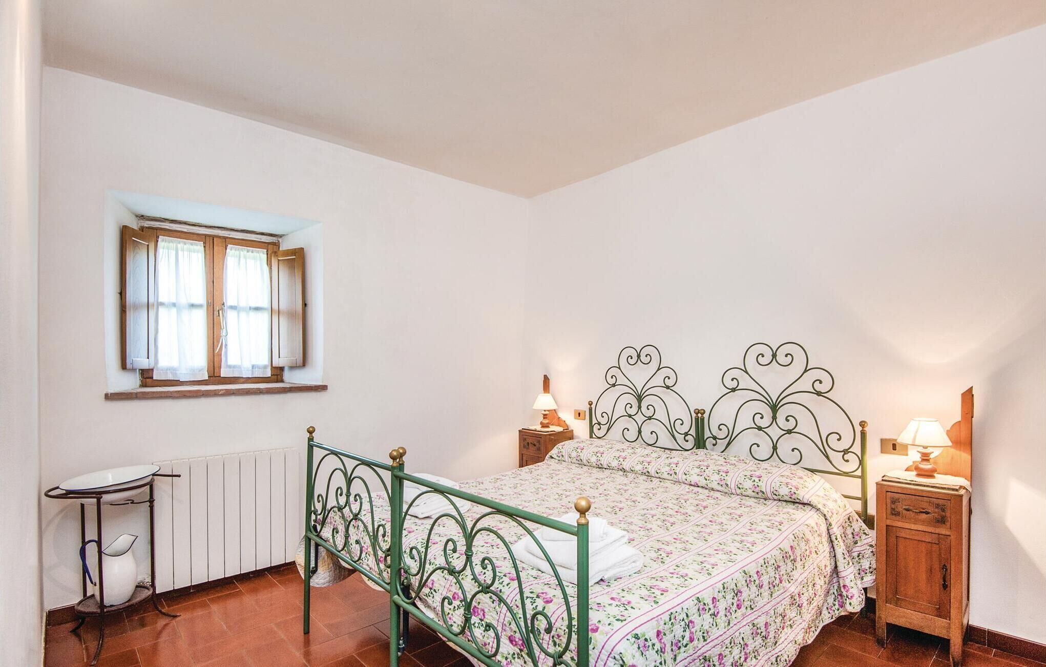 A bedroom with a metal bed frame, a bedside table with a lamp, a radiator, and a window with curtains.