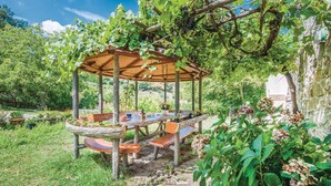 A wooden pergola with a table and benches underneath, surrounded by lush greenery and vines. - Amazing home in Arcidosso GR (Arcidosso GR)