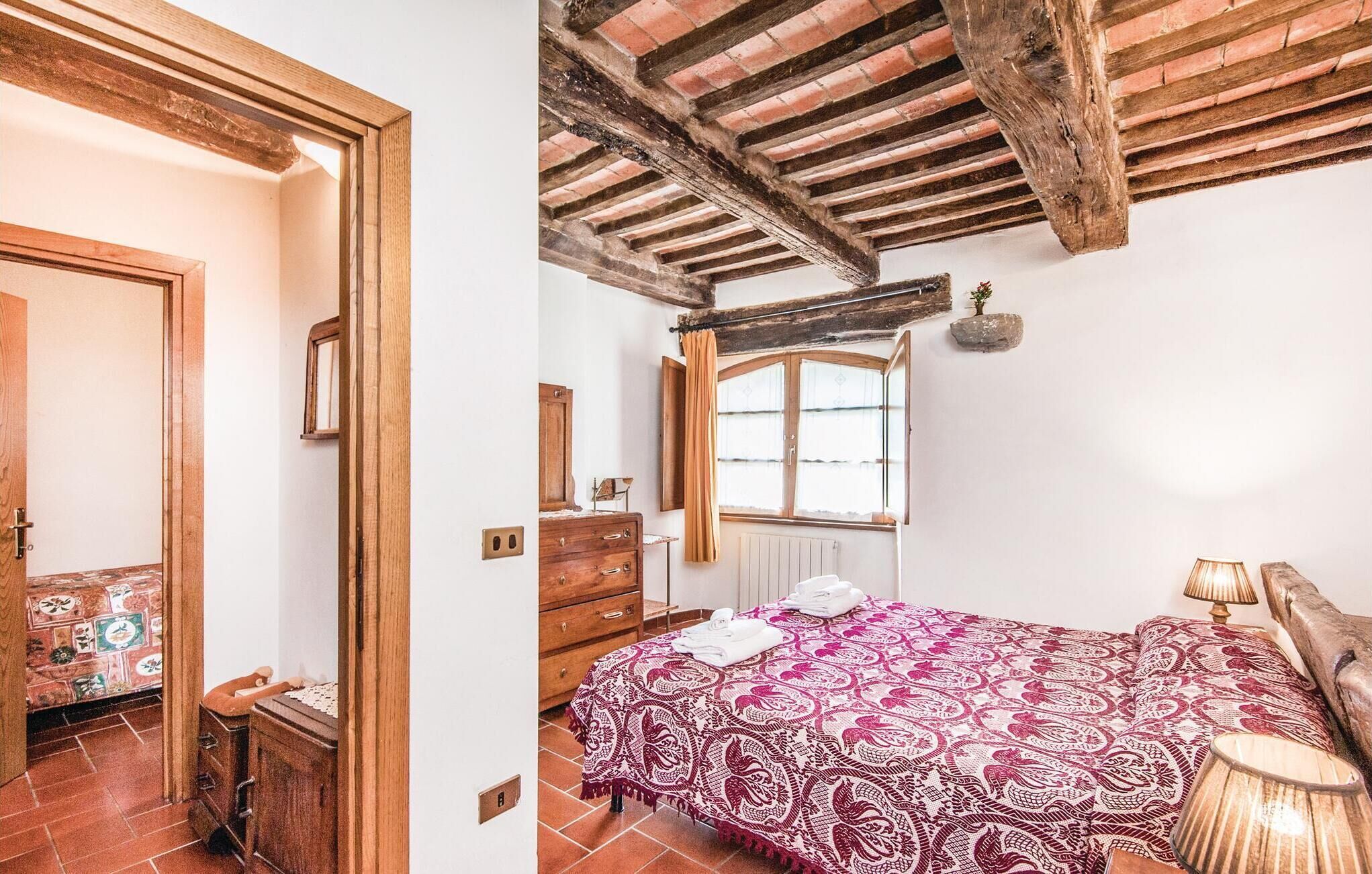 Ein Schlafzimmer mit Holzbalkendecke, einem Bett mit gemustertem Überwurf, einem Schminktisch und einem Fenster mit Vorhängen.