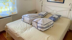 A room with a bed, two pillows, a window with a curtain, and two framed pictures on the wall.