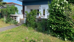 A modern two-story house with a blue roof and white exterior walls, surrounded by lush greenery and a well-maintained garden.