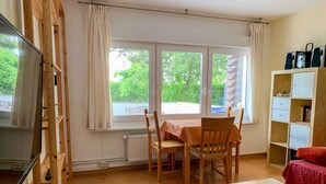 A room with a wooden table and chairs, a TV, a bookshelf, and a window with curtains.