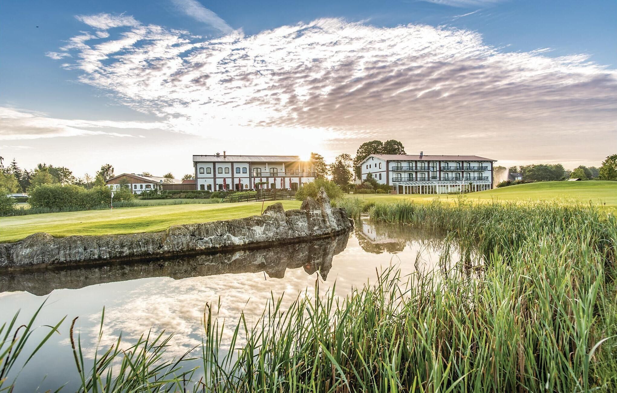 Ett hotell vid sjön med en spegelblank damm, en golfbana och en stor byggnad med många fönster och balkonger.