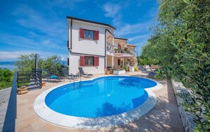 Una casa de dos plantas con piscina, muebles de exterior y vistas al mar.