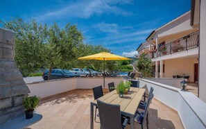 Un patio al aire libre con una mesa y sillas, un paraguas amarillo y una piscina al fondo.