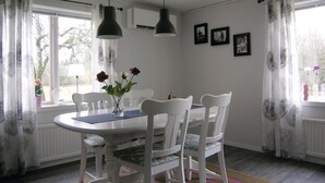 Comedor con una mesa y sillas blancas, un jarrón con flores y una ventana con cortinas.