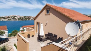 Un bâtiment avec un toit recouvert de tuiles rouges, un balcon agrémenté de meubles d’extérieur et une antenne parabolique.