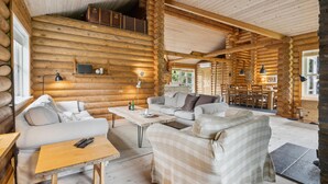 A log cabin interior with a living area featuring sofas, a coffee table, and a dining table. - Lovely home in Stege with sauna (Stege)