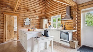 A log cabin kitchen with a central island, white cabinetry, a stove, and a large window. - Lovely home in Stege with sauna (Stege)