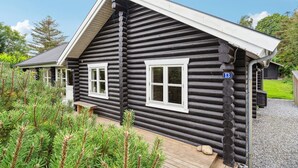 A log cabin with two windows, a wooden deck, and a gravel driveway. - Lovely home in Stege with sauna (Stege)