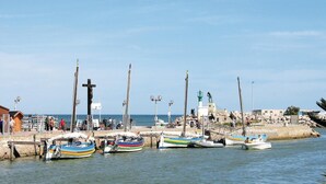 A harbor with boats docked, a lighthouse, and a pier with people and buildings in the background.