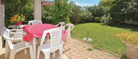 Un patio con una mesa y sillas, rodeado por un jardín y un edificio de techo a ladrillo.