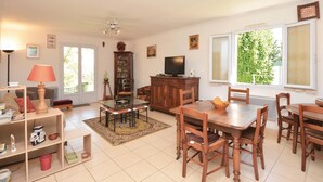 A spacious living room with a dining area, a television, and a large window with a view of greenery.