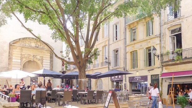 An outdoor café with tables and chairs, surrounded by buildings with balconies and windows.