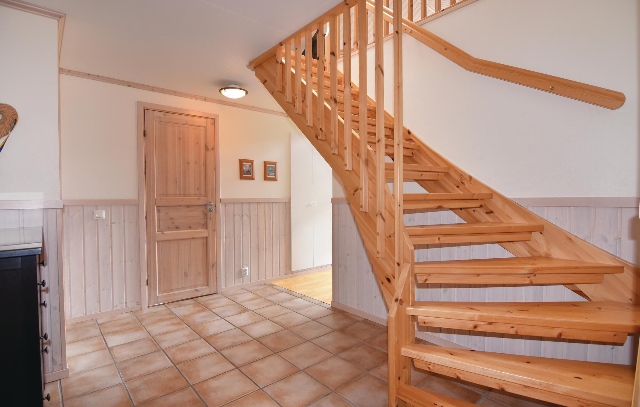 A wooden staircase leading to an upper floor, a door with a handle, and a tiled floor.