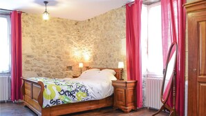 Un dormitorio con pared de piedra, una cama de madera, dos lámparas de noche y un armario de madera.