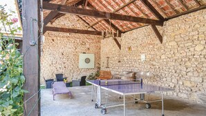 Una habitación rústica con paredes de piedra, mesa de ping pong, sillas de mimbre y dardos.