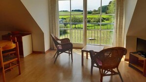 A room with a large window, two wicker chairs, a small table, and a TV stand. - Apartment 3 / o. r. - Ruegen-Fewo 47 (Putbus)