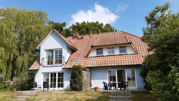 A two-story house with a tiled roof, a balcony, and a small patio area with outdoor furniture. - Apartment 3 / o. r. - Ruegen-Fewo 47 (Putbus)
