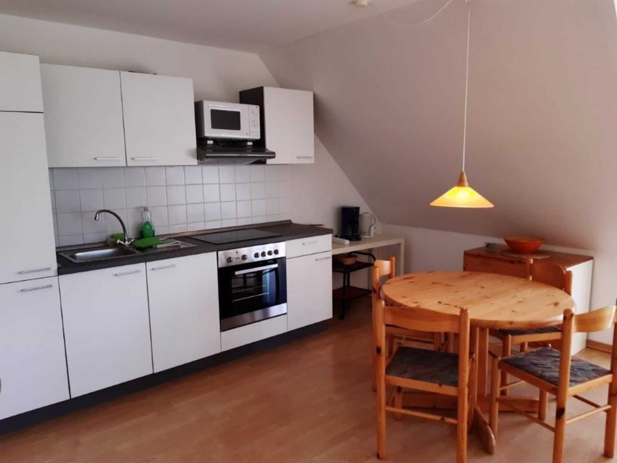 A compact kitchen with white cabinets, a microwave, an oven, and a wooden dining table with chairs.