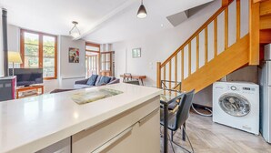 A modern kitchen with a central island, a washing machine, and a wooden staircase. - Appartement jolie vue rivière (Jaulgonne)