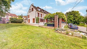 A two-story house with a brick chimney, a stone wall, and a car parked in the driveway. - Appartement jolie vue rivière (Jaulgonne)