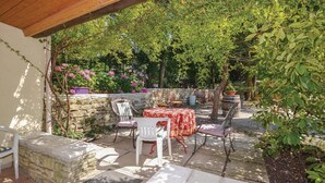 Eine Terrasse im Freien mit Steinmauern, einem Tisch mit rotem Tischlein und mehreren Stühlen.