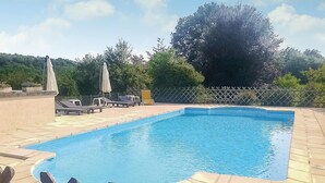 Una piscina rectangular con un borde de baldosas, rodeada de sillones de descanso y sombrillas.