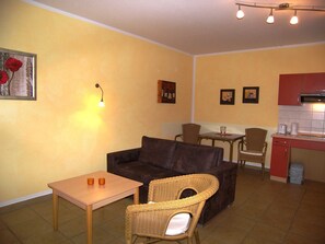 A compact living space with a sofa, a small table, wicker chairs, a kitchenette, and a dining area.