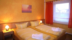 A double room with two beds, a nightstand with a lamp, a painting on the wall, and a window with curtains.