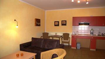 A compact living space with a sofa, dining table, chairs, a kitchenette, and a wall-mounted light fixture.