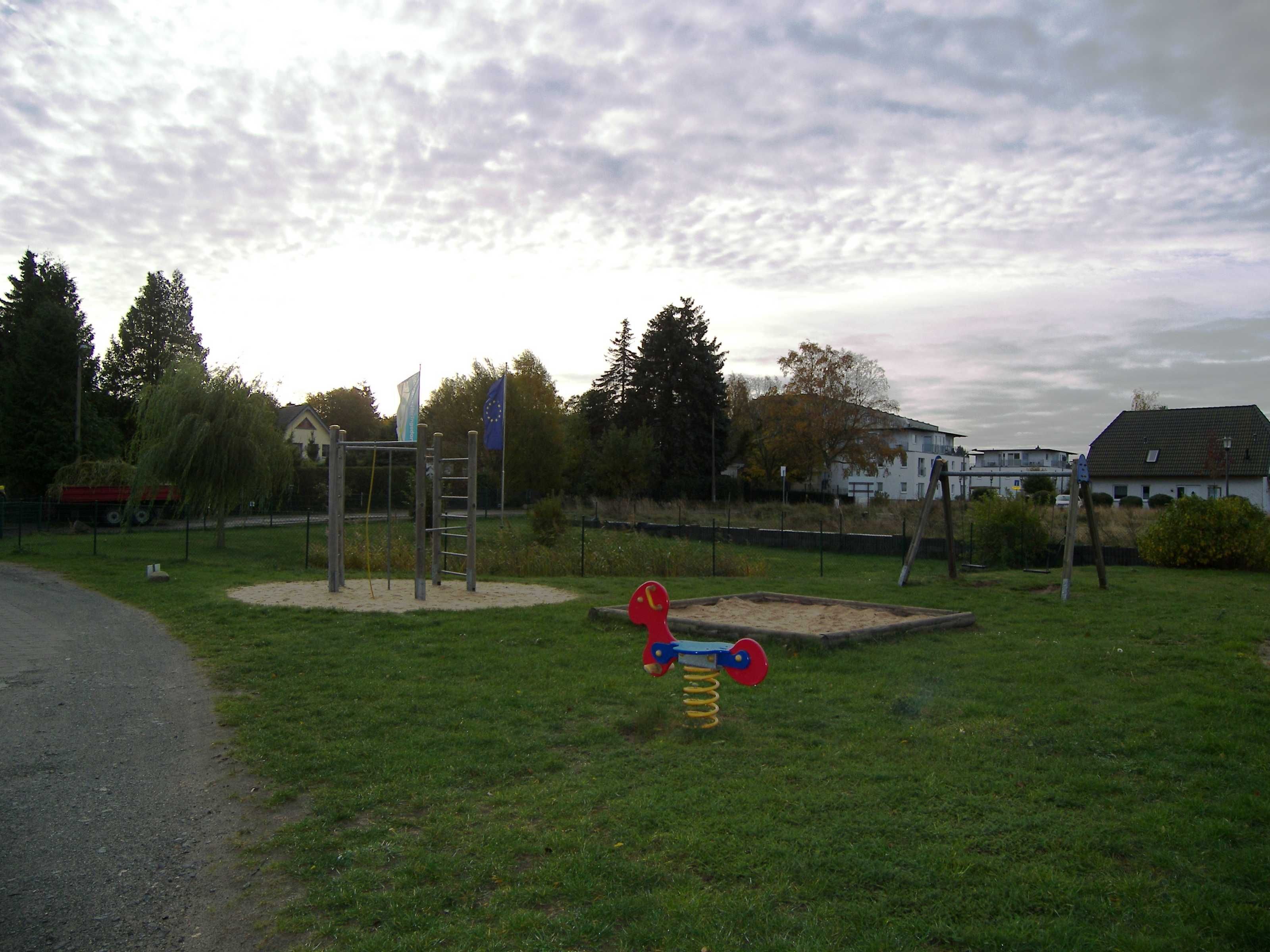A playground with a swing set and a seesaw in a grassy area with trees and buildings in the background.