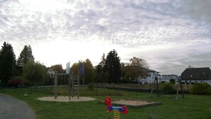 A playground with a swing set and a seesaw in a grassy area with trees and buildings in the background.