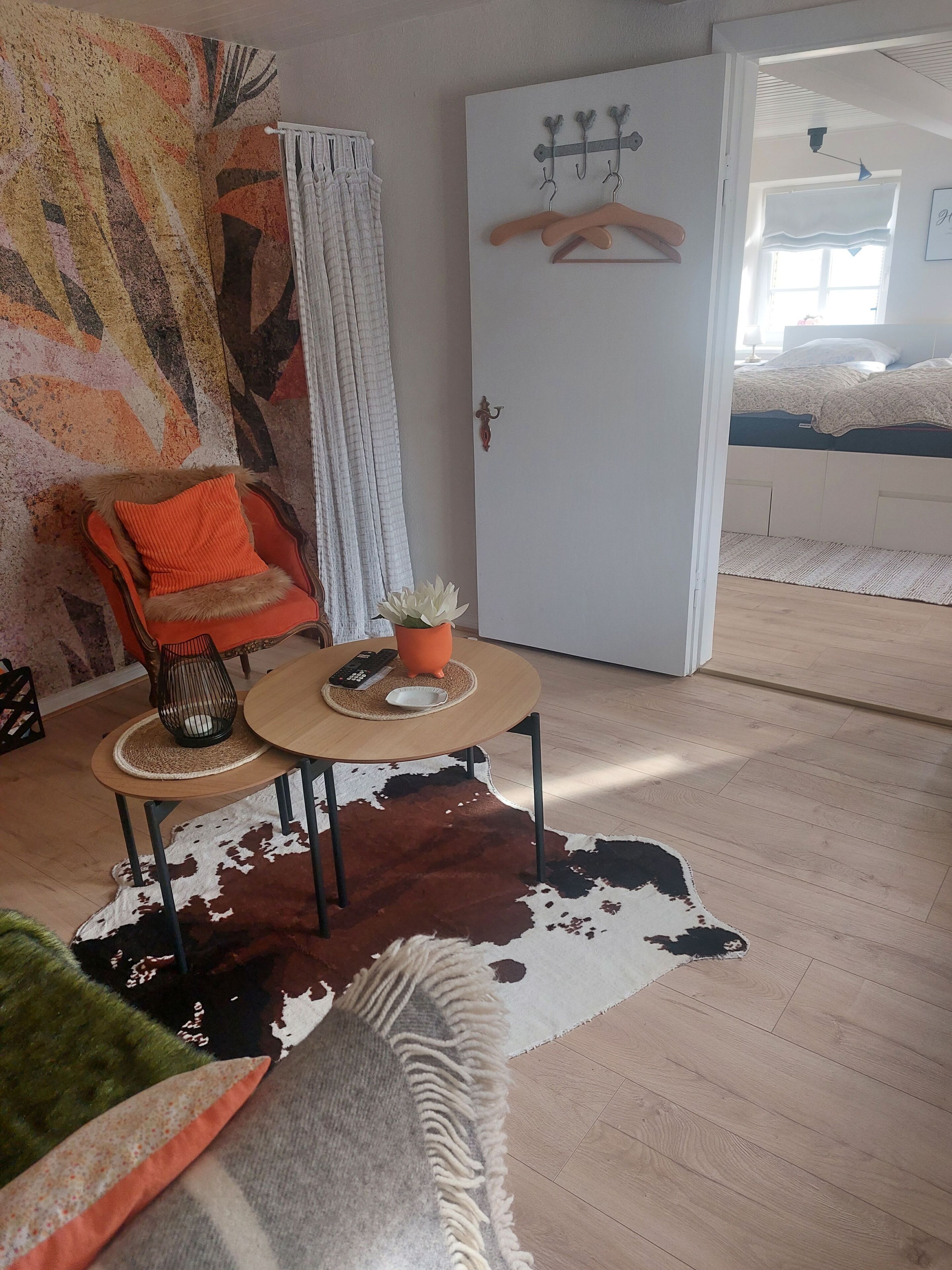 Huoneessa on sänky, tuoli, pöytä, jossa on kasvi, ja lehmännahkamatto.