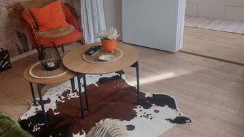 Huoneessa on sänky, tuoli, pöytä, jossa on kasvi, ja lehmännahkamatto.