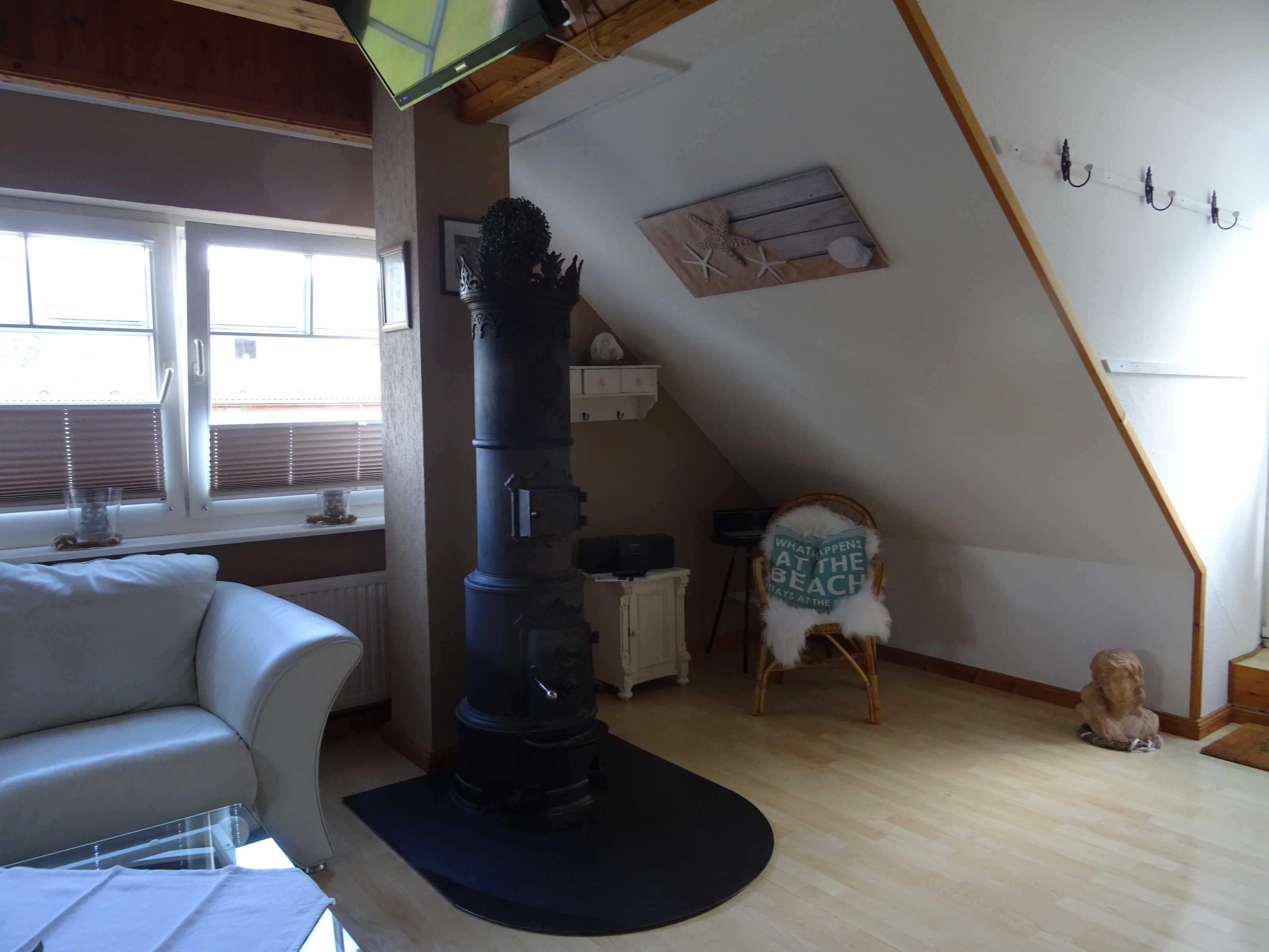 Een kamer met een openhaard, een raam met zonwering, een witte bank, een stoel met een kustthema-kussen en een klein beeld op de vloer.