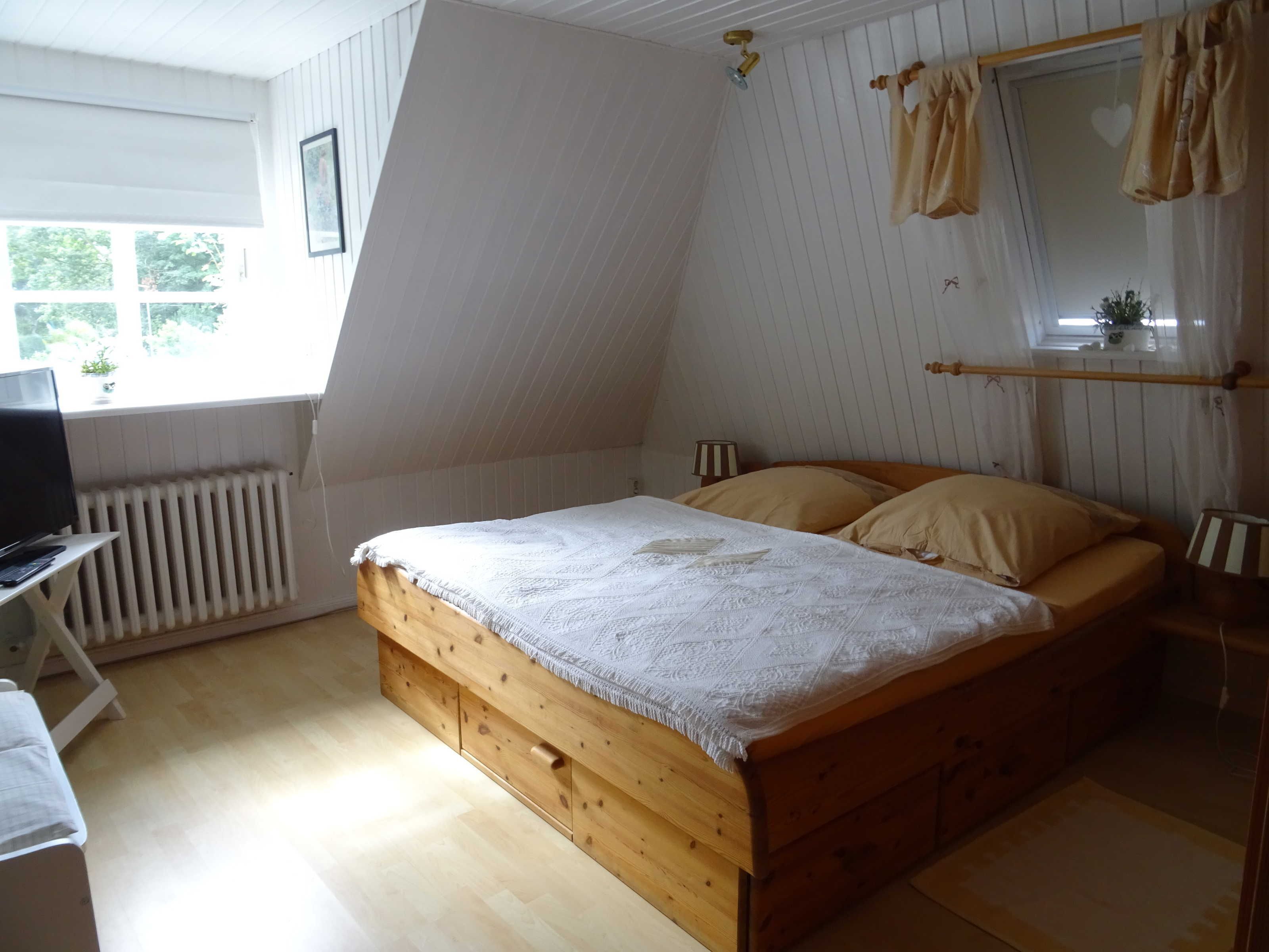 Ein Schlafzimmer mit schrägem Dach, einem Holzbett, einem Schreibtisch und einer Heizung.