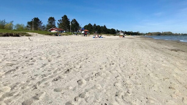 Una playa arenosa con huellas, algunas cabañas de playa y un cielo despejado.