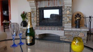 A room with a stone fireplace, a television, and a table with a bottle of wine, glasses, and a vase. - Holiday home with pool and view to Lake Balaton for families (Balatonalmádi)